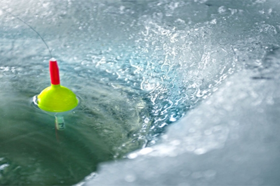 Yellow fishing bobber in the water of an ice hole.