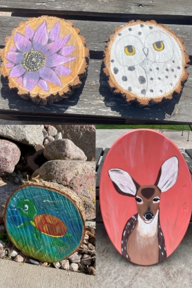 Four paintings on wood slices. One with a purple flower. Another one with a white owl. Then, a wood slice with a painting of a baby turtle underwater and one wood slice with a doe. 