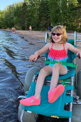 A young girl smiling and entering the water in a beach wheelchair at Big Bay State Park.