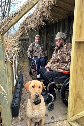 Two gentleman in wheelchairs and a yellow Labrador using an accessible hunting blind at Jackson Marsh Wildlife Area.