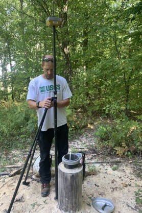 A picture of an United States Geological Survey employee using equipment to measure water level elevation on a groundwater monitoring well.