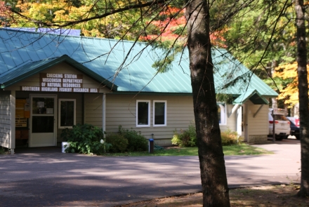 A small building tucked away in the trees, with a sign that says "Checking Station, Escanaba Lake"