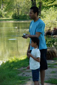 An adult man and a little boy fish along the bank of a waterbody while using loaner tackle.
