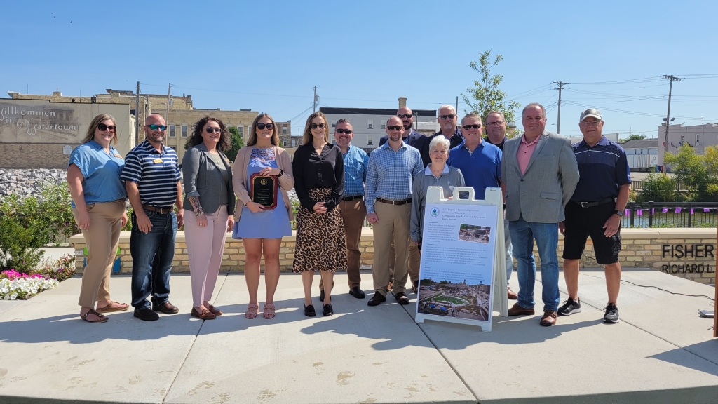 Fourteen different men and women happily posing on a warm sunny day at Watertown's Bentzin Family Town Square with an Environmental Protection Agency award. The group includes the DNR's Jody Irland, Tom Coogan and Jodie Thistle as well as EPA's Sarah Gruza and City of Watertown staff.