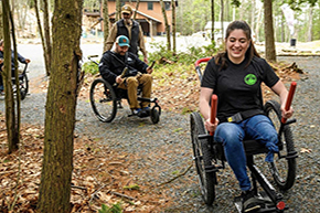 People using GRIT wheelchair bikes on a crushed rock trail in the woods.