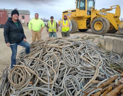 Four crew members standing around a pile of lead service lines that were removed, with a loader tractor in the background.