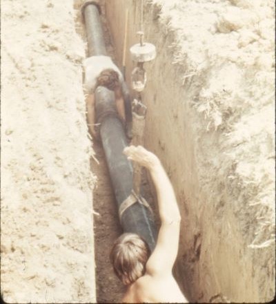 Workers working on a water pipe in the ground without any safety equipment or even a shirt on