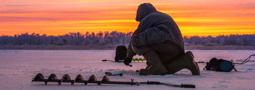 Person knelling on frozen lake at sunset ice fishing.
